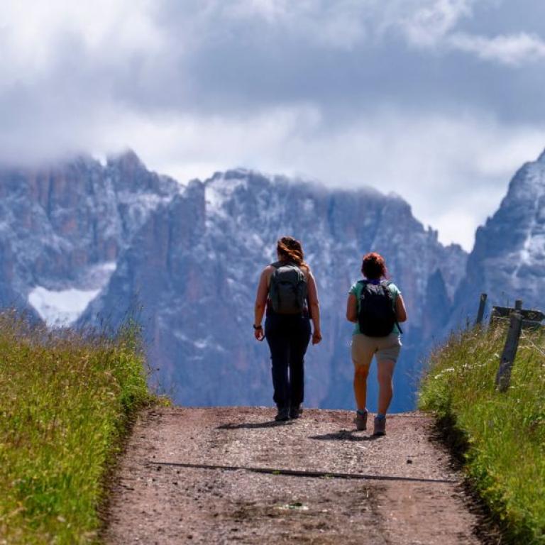 Hikers walking under cloudy skies on the Sentiero del Castagno, surrounded by the dramatic peaks of the Dolomites