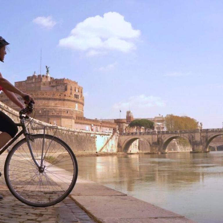 Woman on a bike along the Tiber River at the end of Francigena pilgrimage