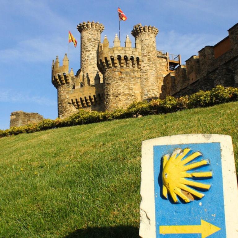 Yellow scallop shell sign marking the Camino de Santiago with a medieval castle in the background