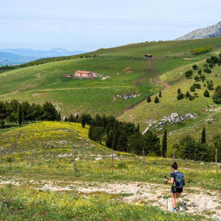 Due escursionisti camminano tra le colline e i pascoli verdi delle Madonie, lungo un tratto della Magna Via Francigena
