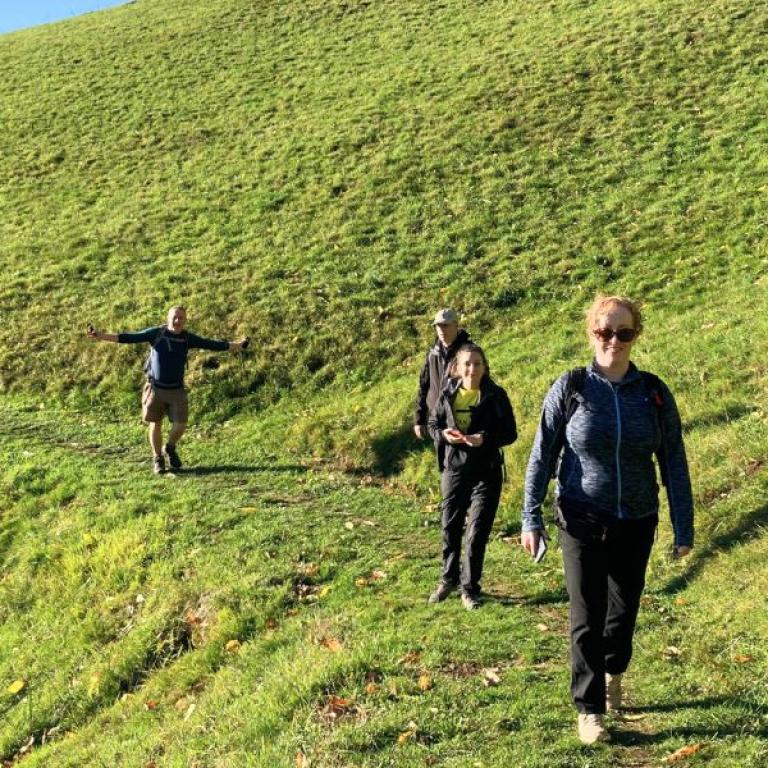 Escursionisti che percorrono un sentiero erboso nelle colline piemontesi durante il Cammino di Oropa