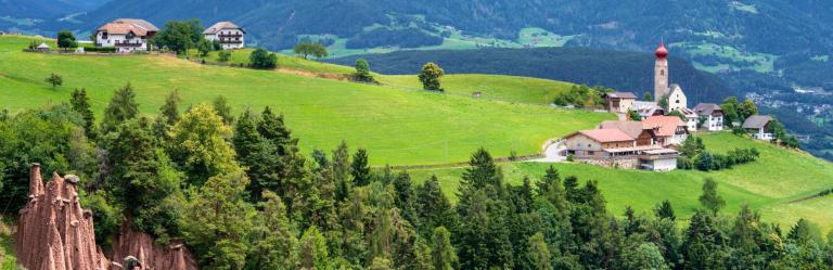 View of the rolling hills and farms along the Sentiero del Castagno in South Tyrol, surrounded by green meadows and mountain landscapes