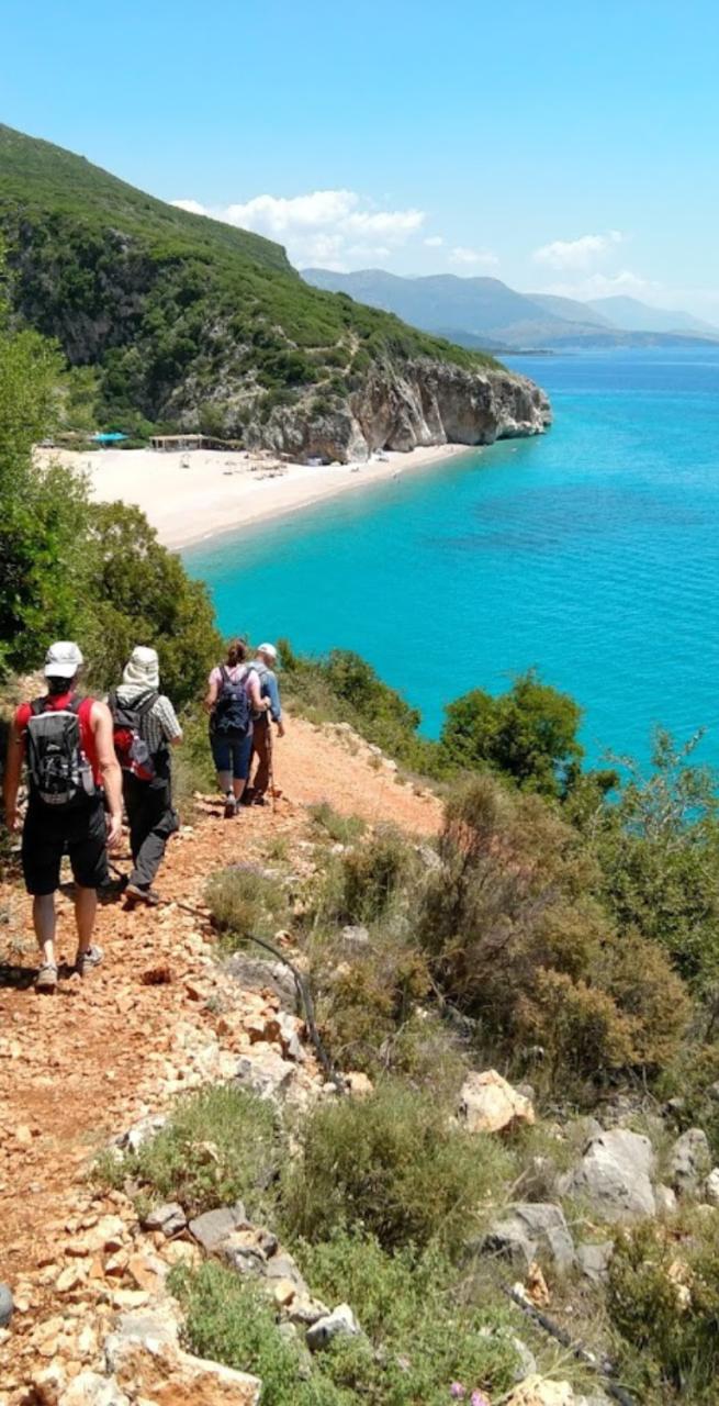 Hikers on a lush coastal trail overlooking the deep blue Ionian Sea.