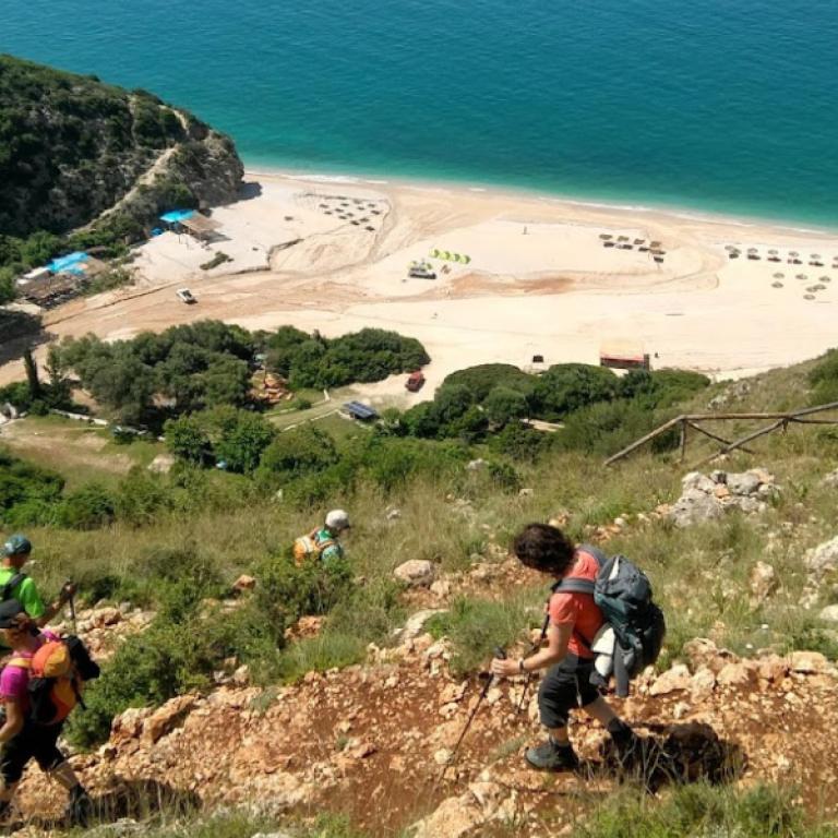 Hikers descending a green hillside toward a secluded beach on the Albania Coastal trail.