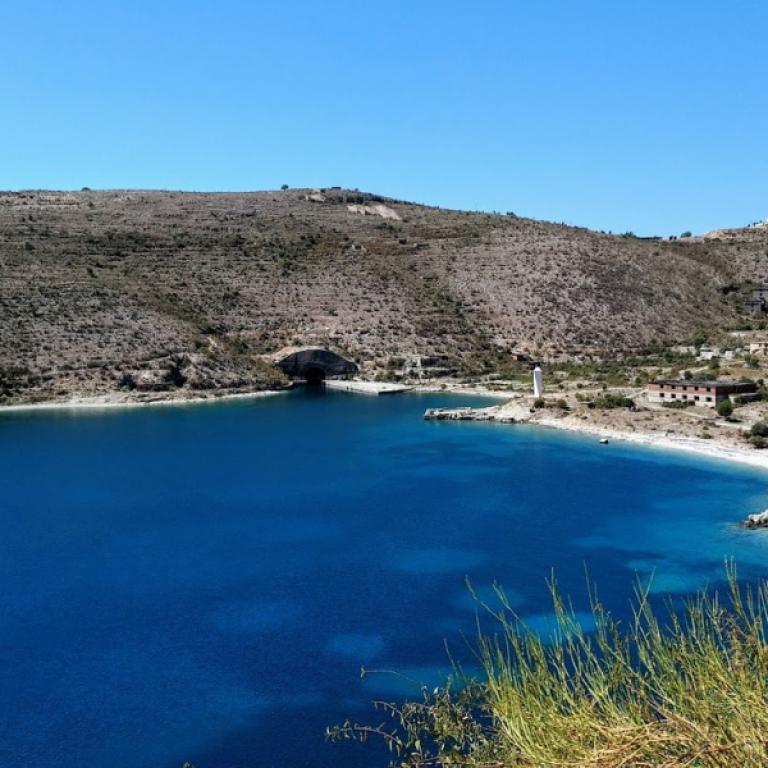Secluded cove with turquoise water and a small coastal settlement along the Albania Coastal trail.