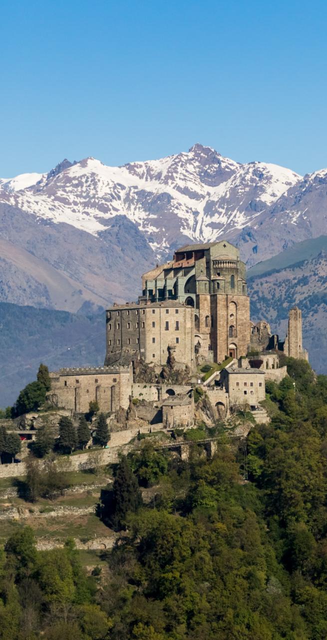 Sacra di San Michele perched above the Susa Valley with snowy alpine peaks and tree branches