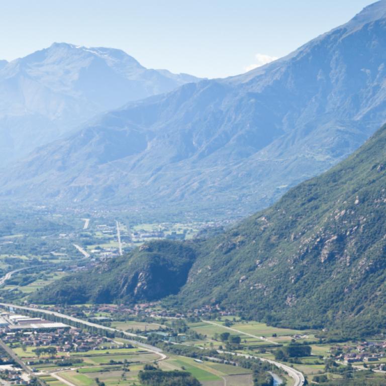 Panoramic view of the Susa Valley with winding road and green mountains along the Via Francigena.