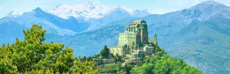 Sacra di San Michele perched above the Susa Valley with snowy alpine peaks and tree branches